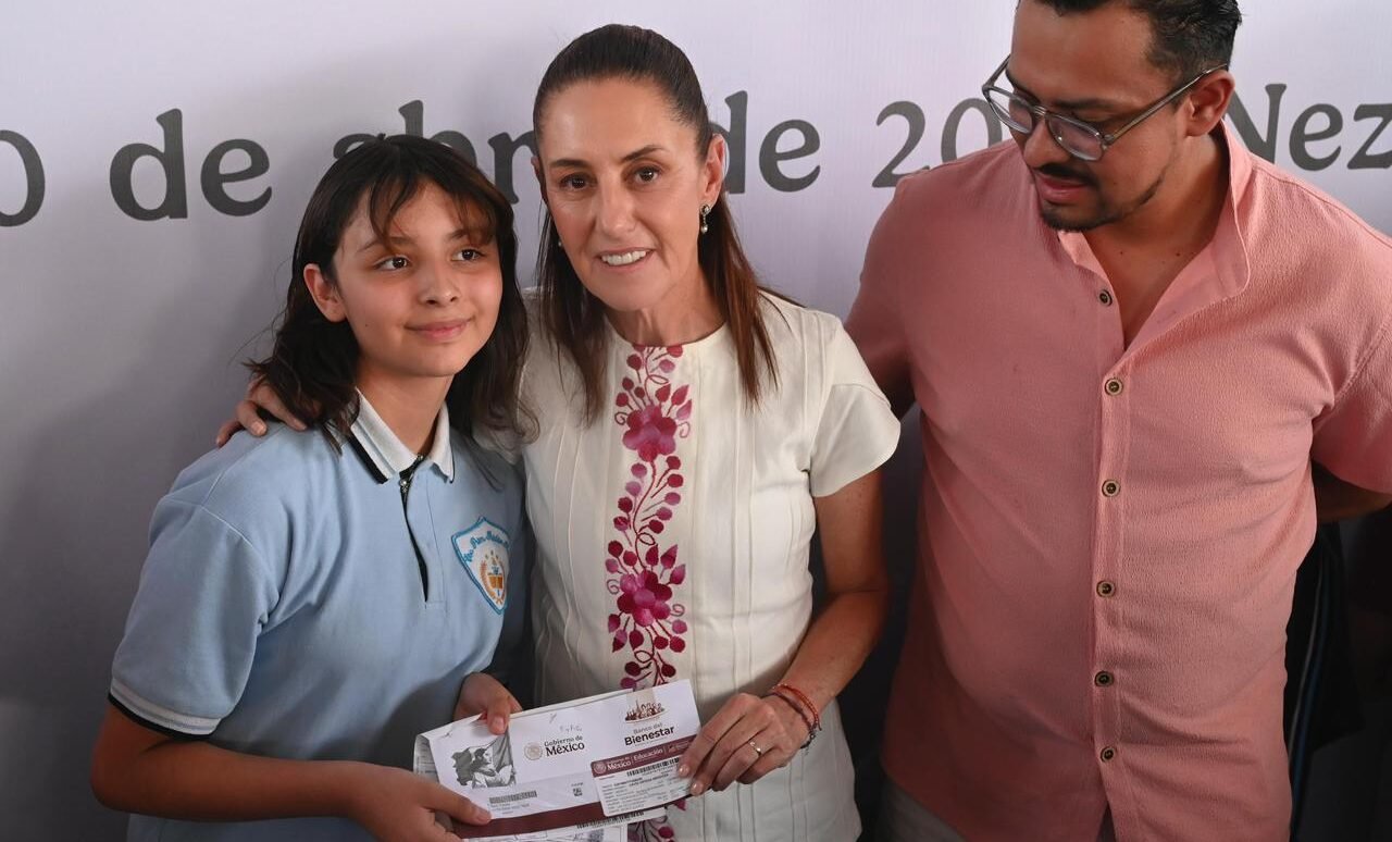 Una estudiante recibe un apoyo de la Beca Rita Cetina junto a dos adultos durante un acto oficial.