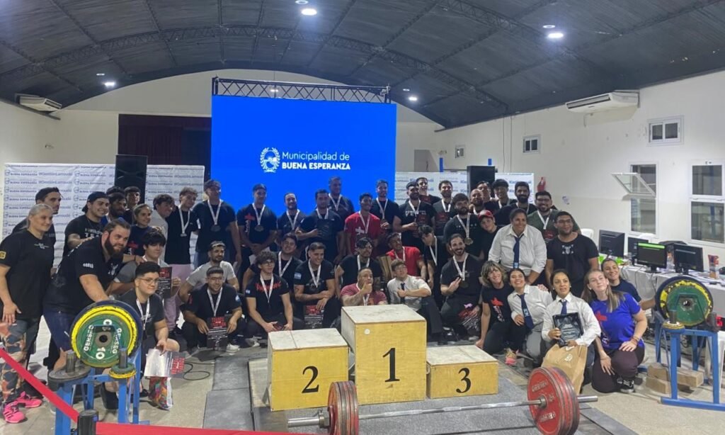 Atletas y organizadores posan junto al podio y las pesas durante el Torneo Apertura de powerlifting en Buena Esperanza.