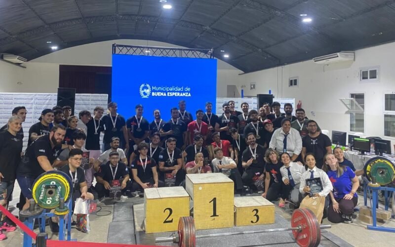 Atletas y organizadores posan junto al podio y las pesas durante el Torneo Apertura de powerlifting en Buena Esperanza.