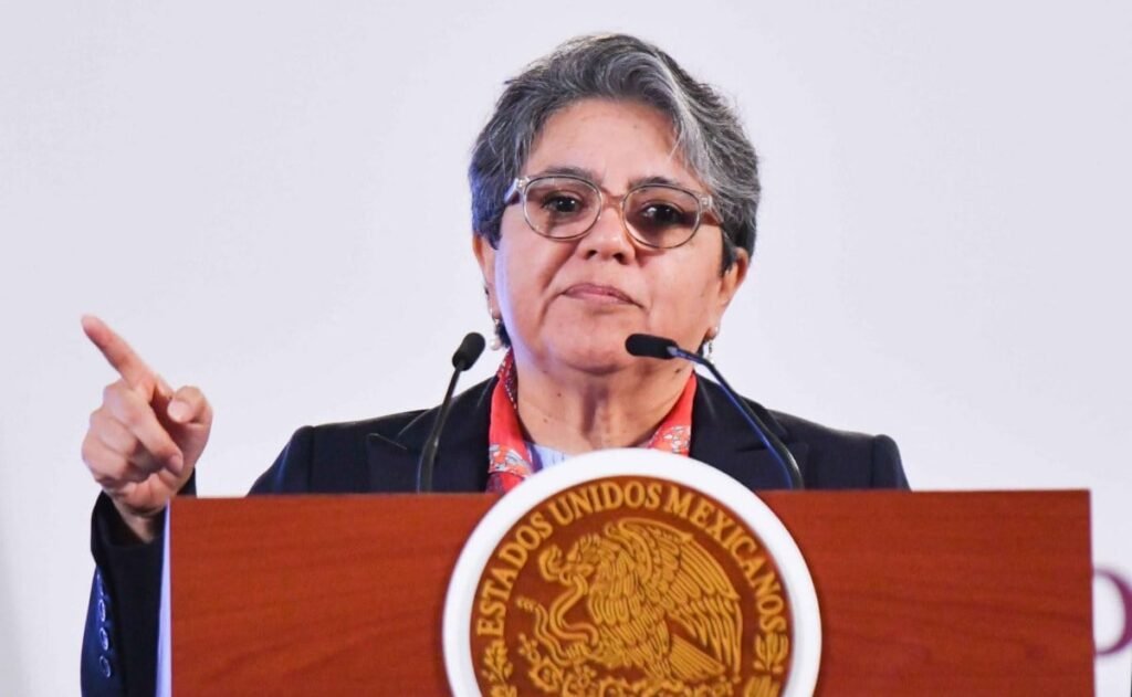 Fotografía contextual de una funcionaria ante el emblema de los Estados Unidos Mexicanos, durante una intervención pública.