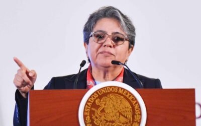 Fotografía contextual de una funcionaria ante el emblema de los Estados Unidos Mexicanos, durante una intervención pública.