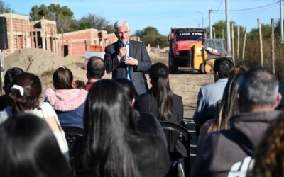 El gobernador Claudio Poggi habla ante vecinos durante una recorrida por el predio de las viviendas en construcción, con casas de ladrillo y maquinaria al fondo.