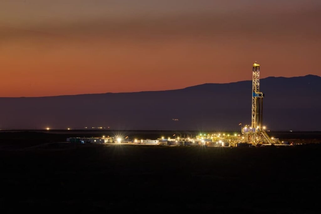 Imagen de archivo de una operación petrolera en Vaca Muerta, con una torre de perforación iluminada al atardecer.