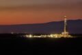 Imagen de archivo de una operación petrolera en Vaca Muerta, con una torre de perforación iluminada al atardecer.