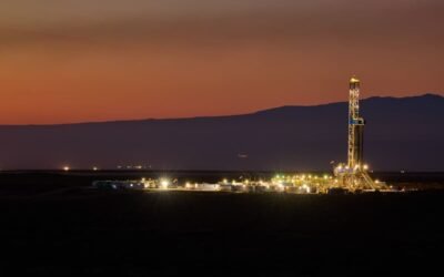 Imagen de archivo de una operación petrolera en Vaca Muerta, con una torre de perforación iluminada al atardecer.