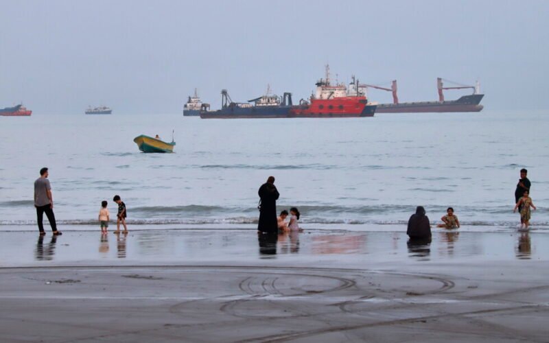 Imagen de archivo de personas en una playa frente a buques comerciales anclados en el estrecho de Ormuz, cerca de Bandar Abbas, Irán.
