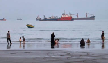 Imagen contextual de personas en una playa frente a buques anclados en el estrecho de Ormuz, cerca de Bandar Abbas, Irán.