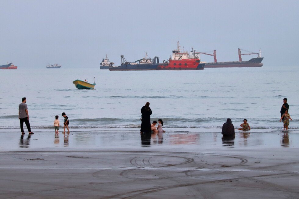Imagen contextual de personas en una playa frente a buques anclados en el estrecho de Ormuz, cerca de Bandar Abbas, Irán.