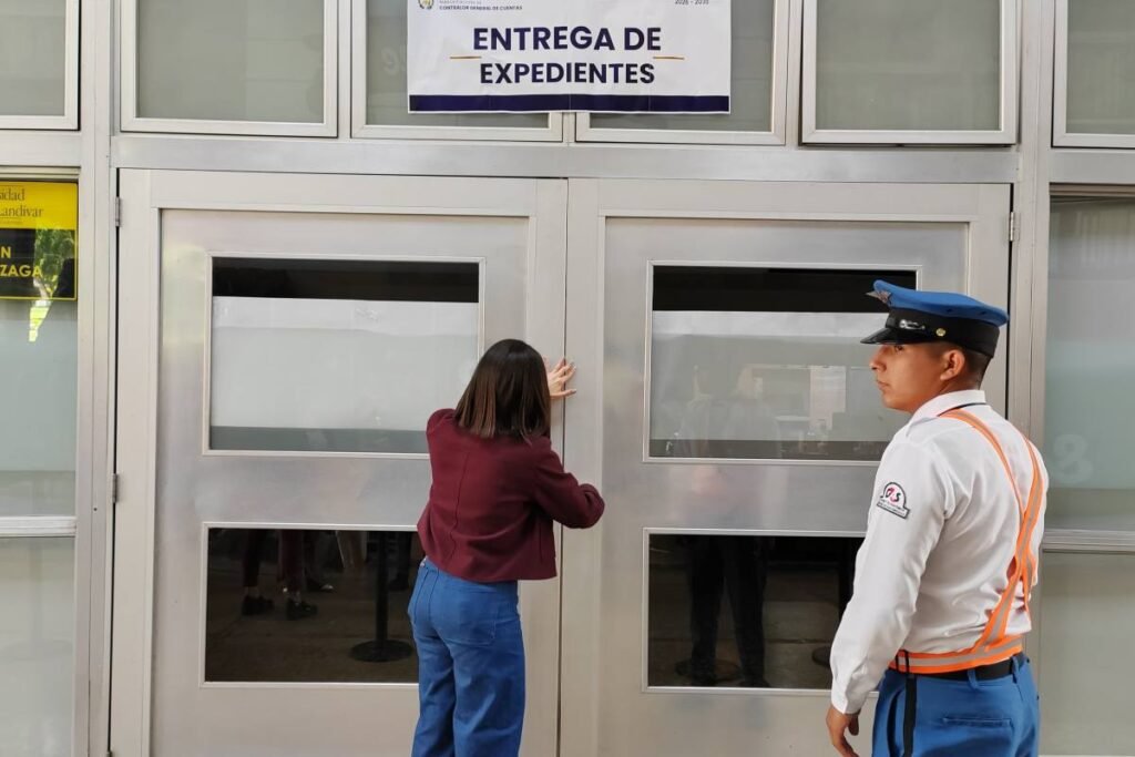 Una mujer entrega documentación en el área de recepción de expedientes, junto a un agente de seguridad.