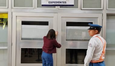 Una mujer entrega documentación en el área de recepción de expedientes, junto a un agente de seguridad.
