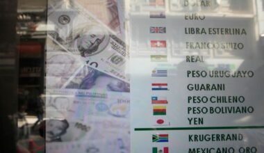 Imagen de archivo de una pizarra de cotizaciones de monedas junto a billetes de dólar.