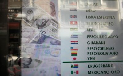 Imagen de archivo de una pizarra de cotizaciones de monedas junto a billetes de dólar.