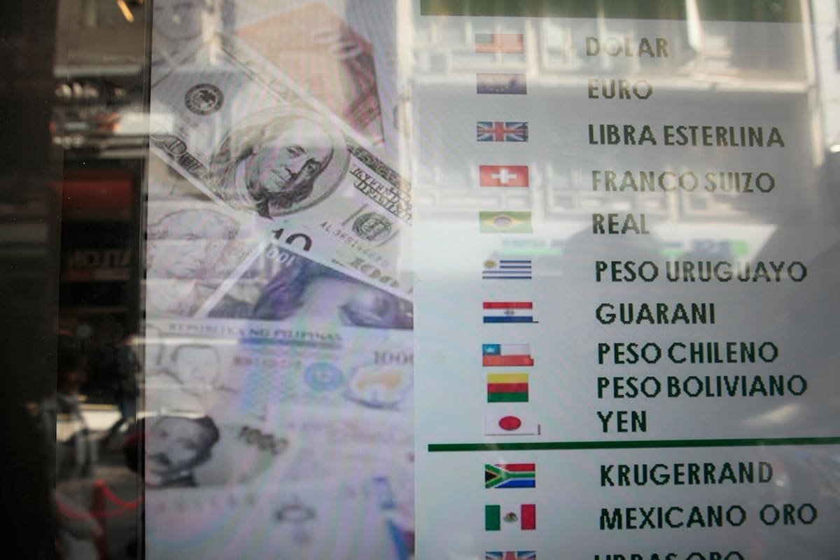 Imagen de archivo de una pizarra de cotizaciones de monedas junto a billetes de dólar.