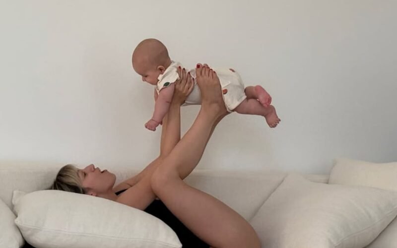 Úrsula Corberó juega con su hijo Dante en un sofá, levantándolo suavemente con las piernas.