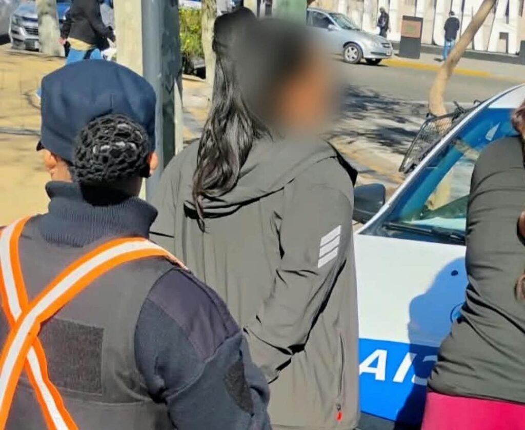 Mujer con el rostro difuminado junto a personal policial y un móvil durante el operativo en San Luis.
