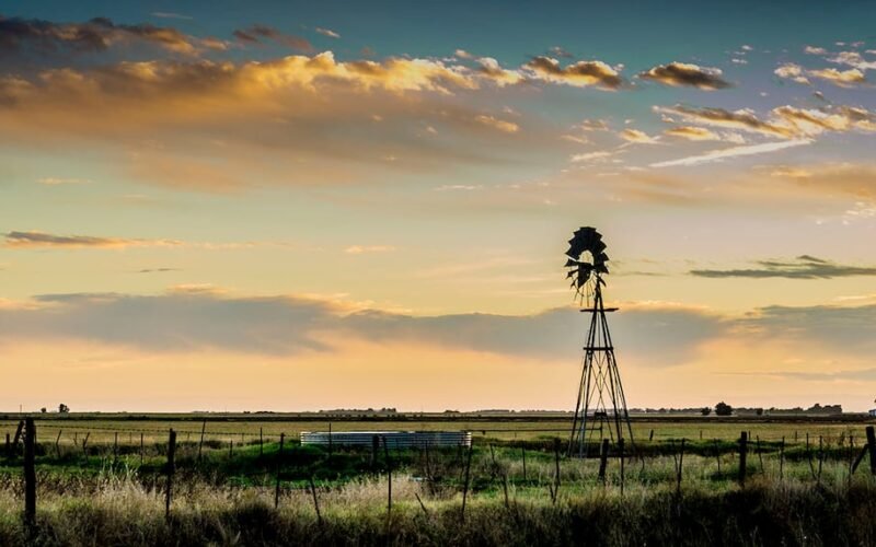 Imagen de archivo de un paisaje rural agrícola al atardecer, con un molino de viento y campos en el horizonte.