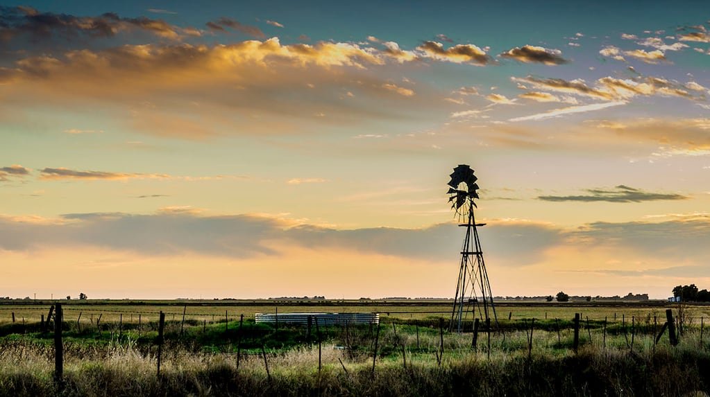 Imagen de archivo de un paisaje rural agrícola al atardecer, con un molino de viento y campos en el horizonte.
