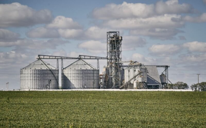 Imagen contextual de una planta de acopio de granos junto a un campo agrícola.