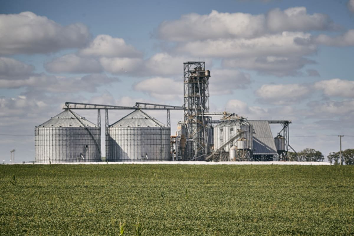 Imagen contextual de una planta de acopio de granos junto a un campo agrícola.