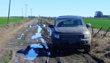 Camino rural anegado y deteriorado, con un vehículo detenido entre charcos y barro.