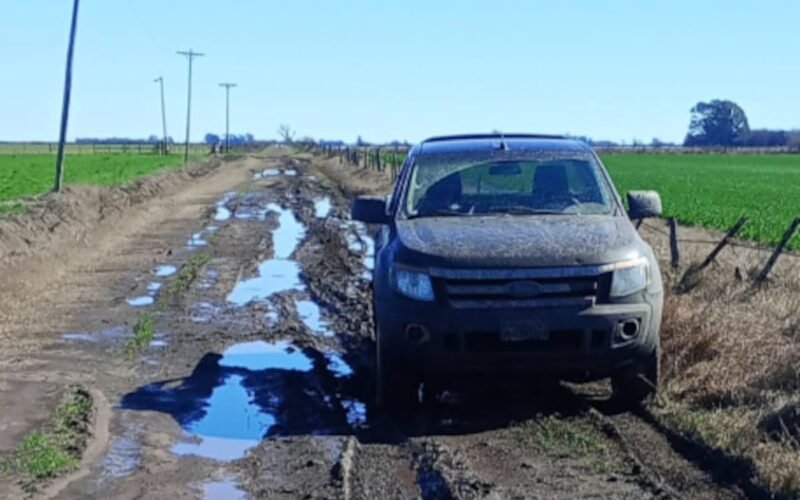Camino rural anegado y deteriorado, con un vehículo detenido entre charcos y barro.