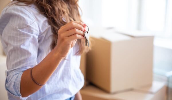 Imagen ilustrativa de una joven sosteniendo las llaves de una vivienda junto a cajas de mudanza.