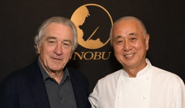 Robert De Niro y el chef Nobu Matsuhisa posan juntos frente al logo de Nobu.