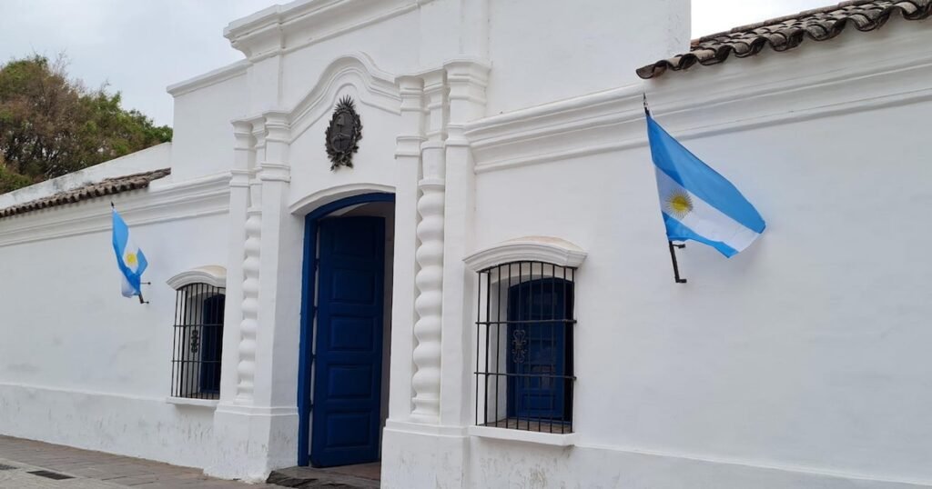 Imagen contextual de la Casa Histórica de la Independencia en San Miguel de Tucumán, con banderas argentinas en su fachada.