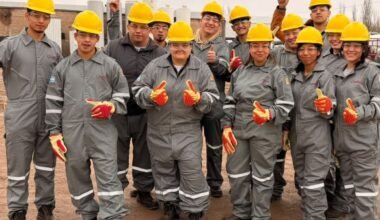 Jóvenes participantes de una capacitación para ingresar a la industria petrolera posan con cascos y ropa de seguridad industrial.