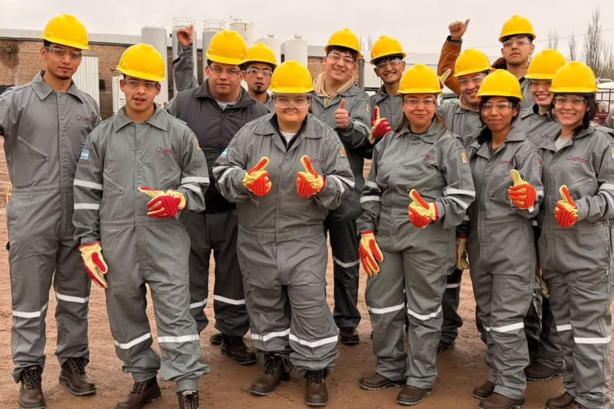 Jóvenes participantes de una capacitación para ingresar a la industria petrolera posan con cascos y ropa de seguridad industrial.