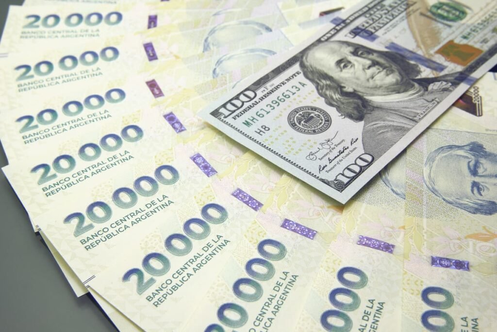Imagen contextual de billetes argentinos de 20.000 pesos junto a billetes de 100 dólares.