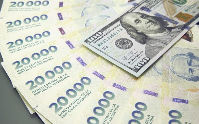 Imagen contextual de billetes argentinos de 20.000 pesos junto a billetes de 100 dólares.