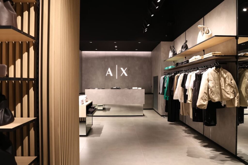 Interior del nuevo local de Armani Exchange, con prendas y accesorios exhibidos y el logotipo A|X en la pared.