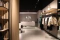 Interior del nuevo local de Armani Exchange, con prendas y accesorios exhibidos y el logotipo A|X en la pared.