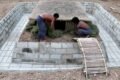 Dos personas trabajan en una vivienda semienterrada rodeada por una pileta en construcción.