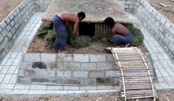 Dos personas trabajan en una vivienda semienterrada rodeada por una pileta en construcción.