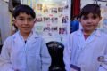 Dos estudiantes de guardapolvo posan junto a una exposición de proyectos en la Feria de Ciencias.