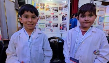 Dos estudiantes de guardapolvo posan junto a una exposición de proyectos en la Feria de Ciencias.