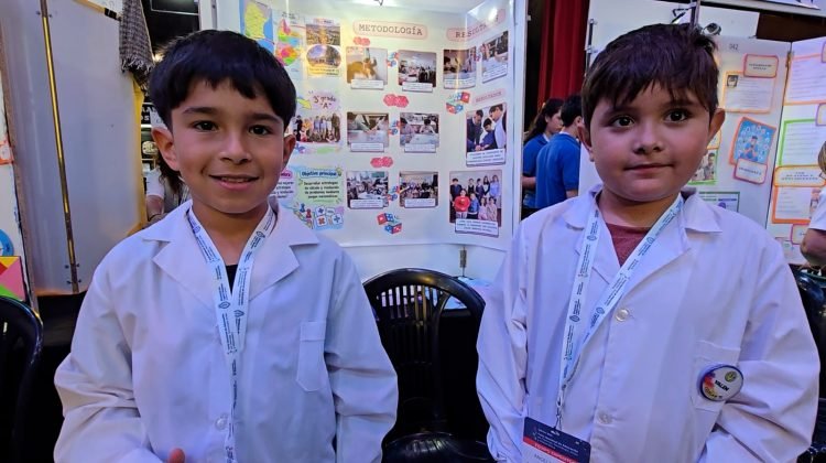 Dos estudiantes de guardapolvo posan junto a una exposición de proyectos en la Feria de Ciencias.