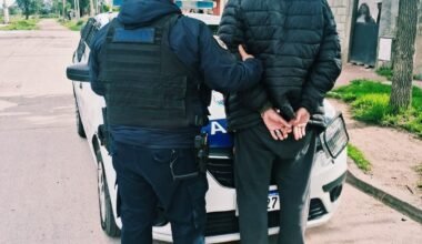 Un agente acompaña a un hombre detenido junto a un patrullero.