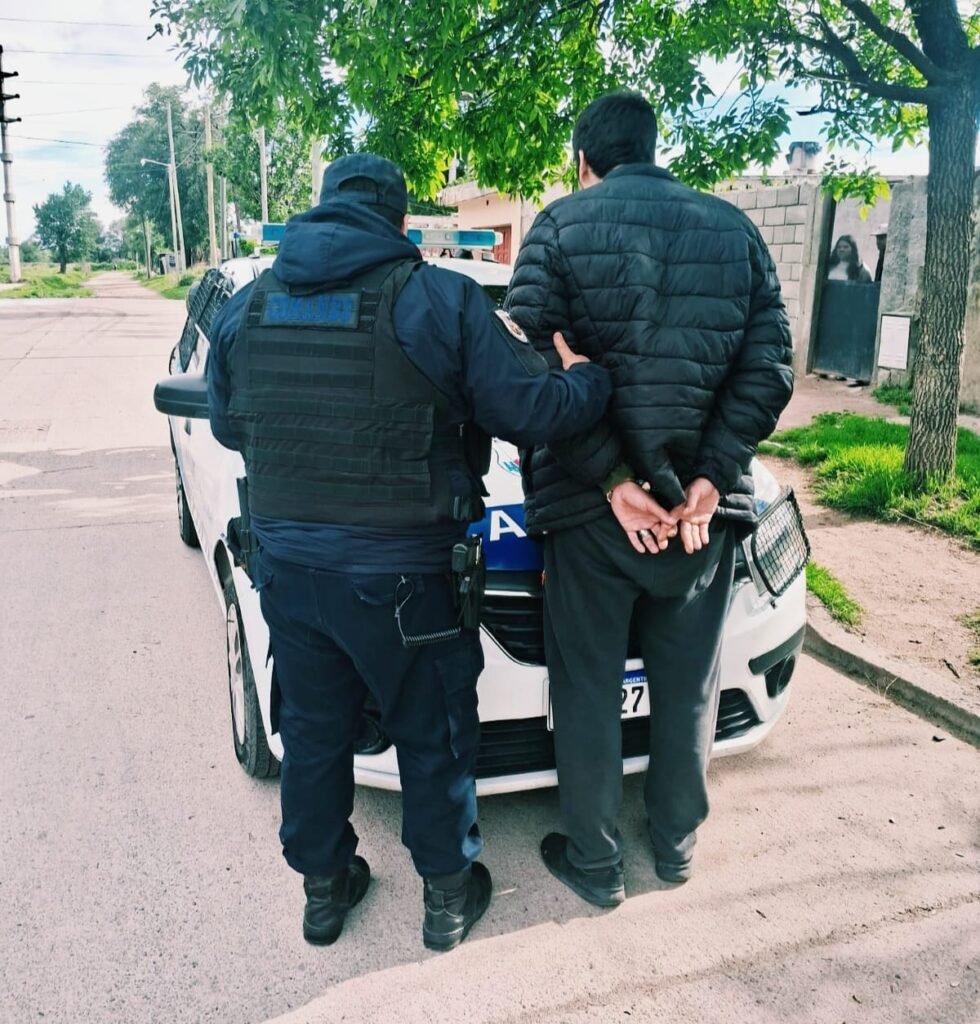 Un agente acompaña a un hombre detenido junto a un patrullero.
